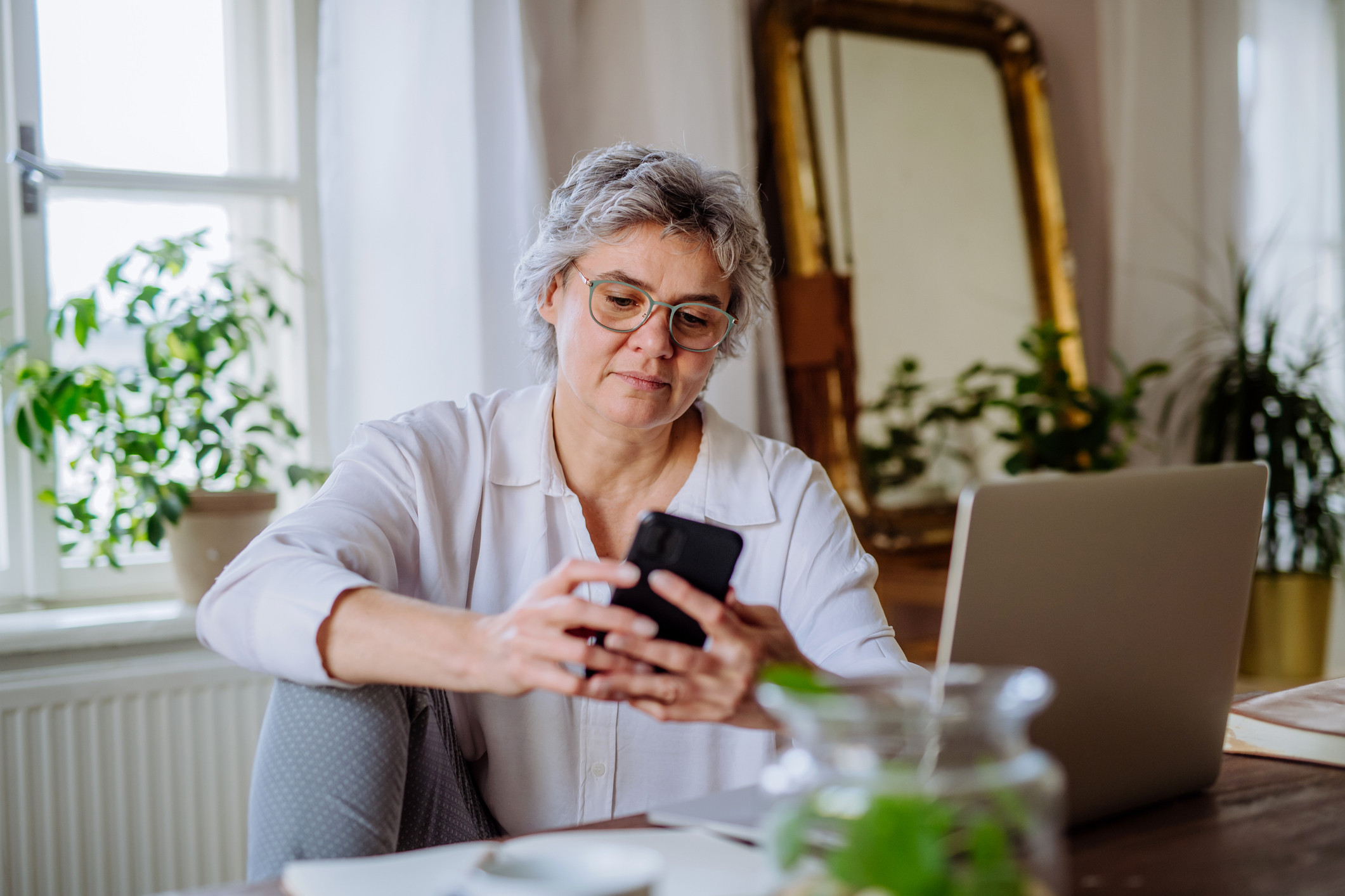 A woman at home using her smartphone and laptop simultaneously to research travel deals.