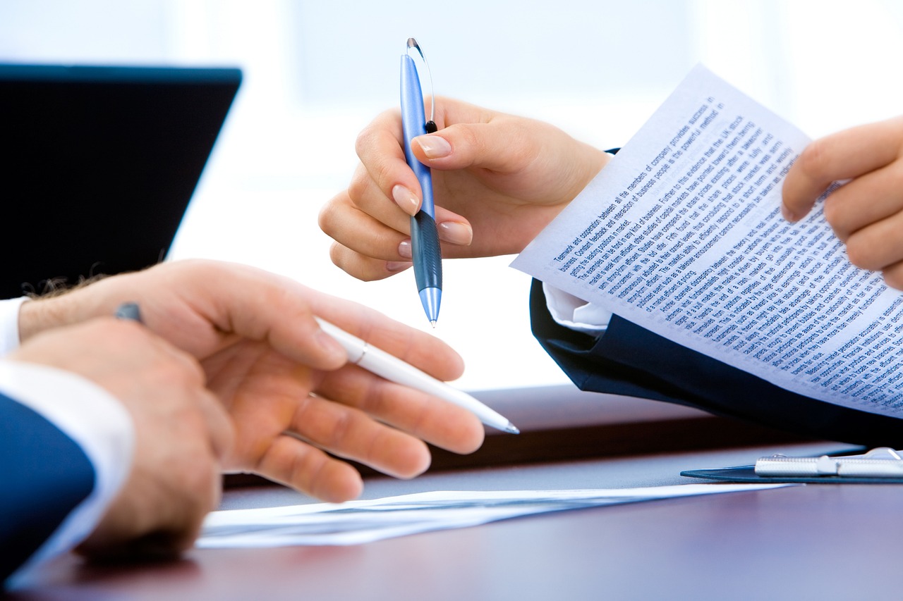 A magnifying glass hovering over a paper document with lists of financial data.
