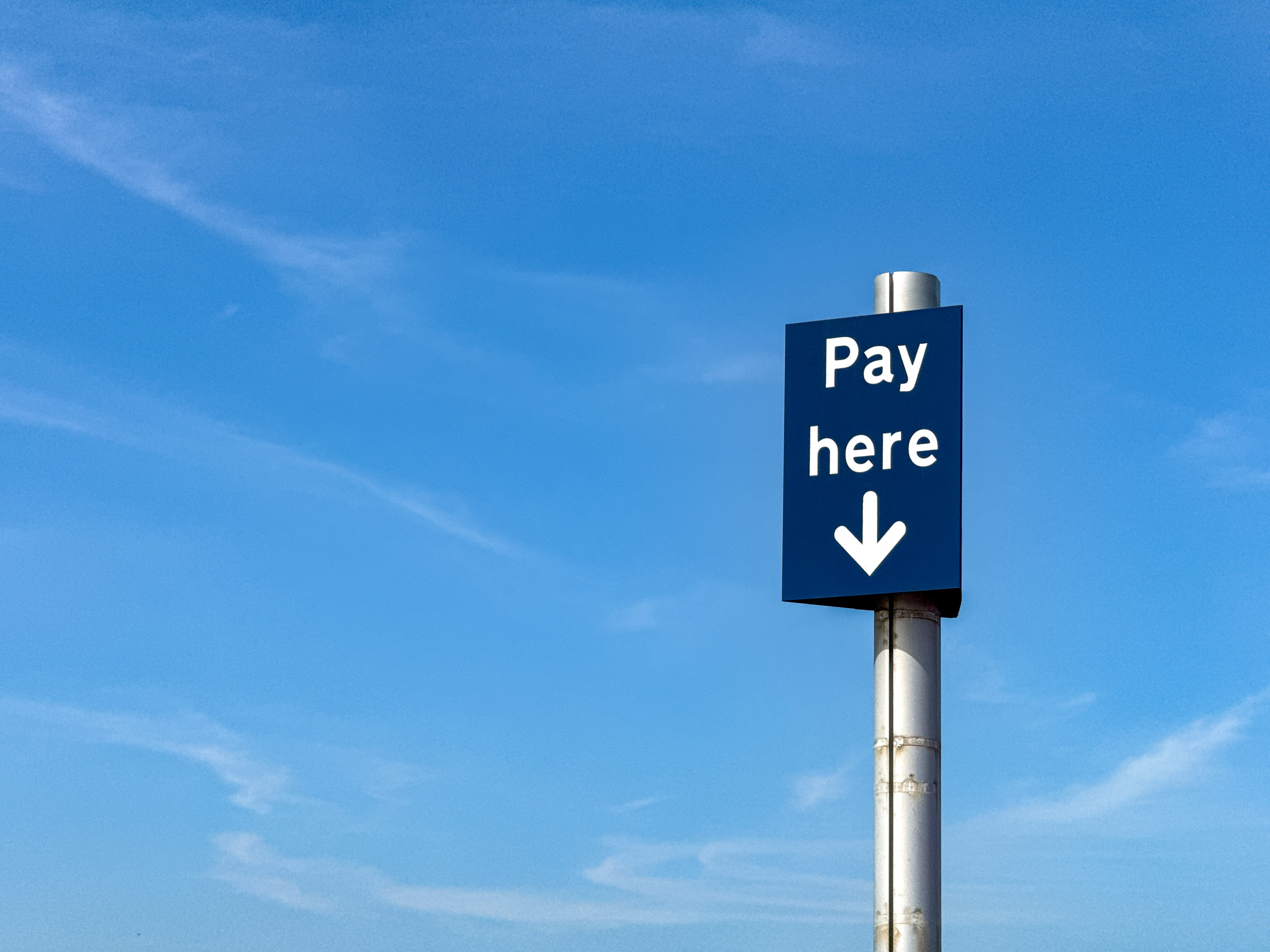 A 'Pay Here' sign in a parking lot set against a clear blue sky.