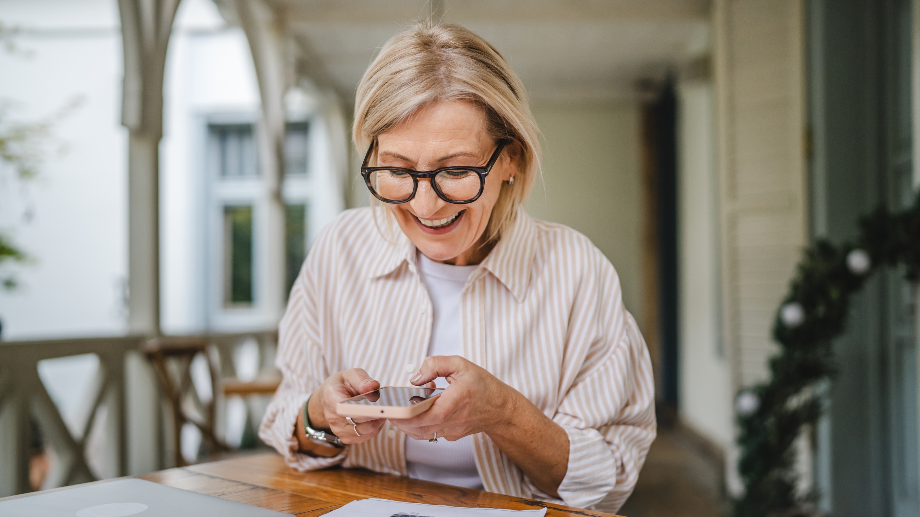 A smiling senior woman relaxing on a porch while checking her mobile phone.