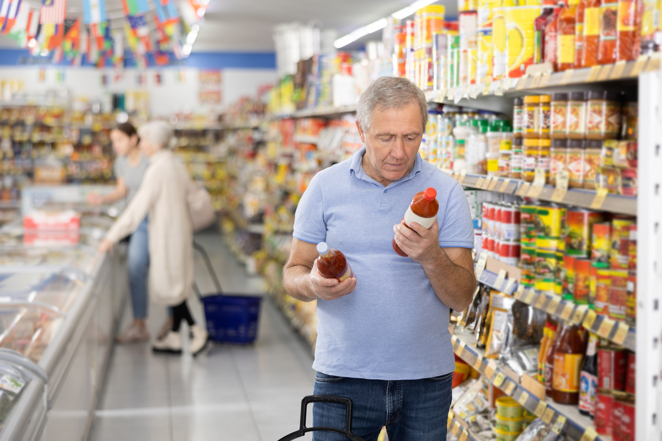 A man wearing a plaid shirt examines product labels on a grocery store shelf to compare items.