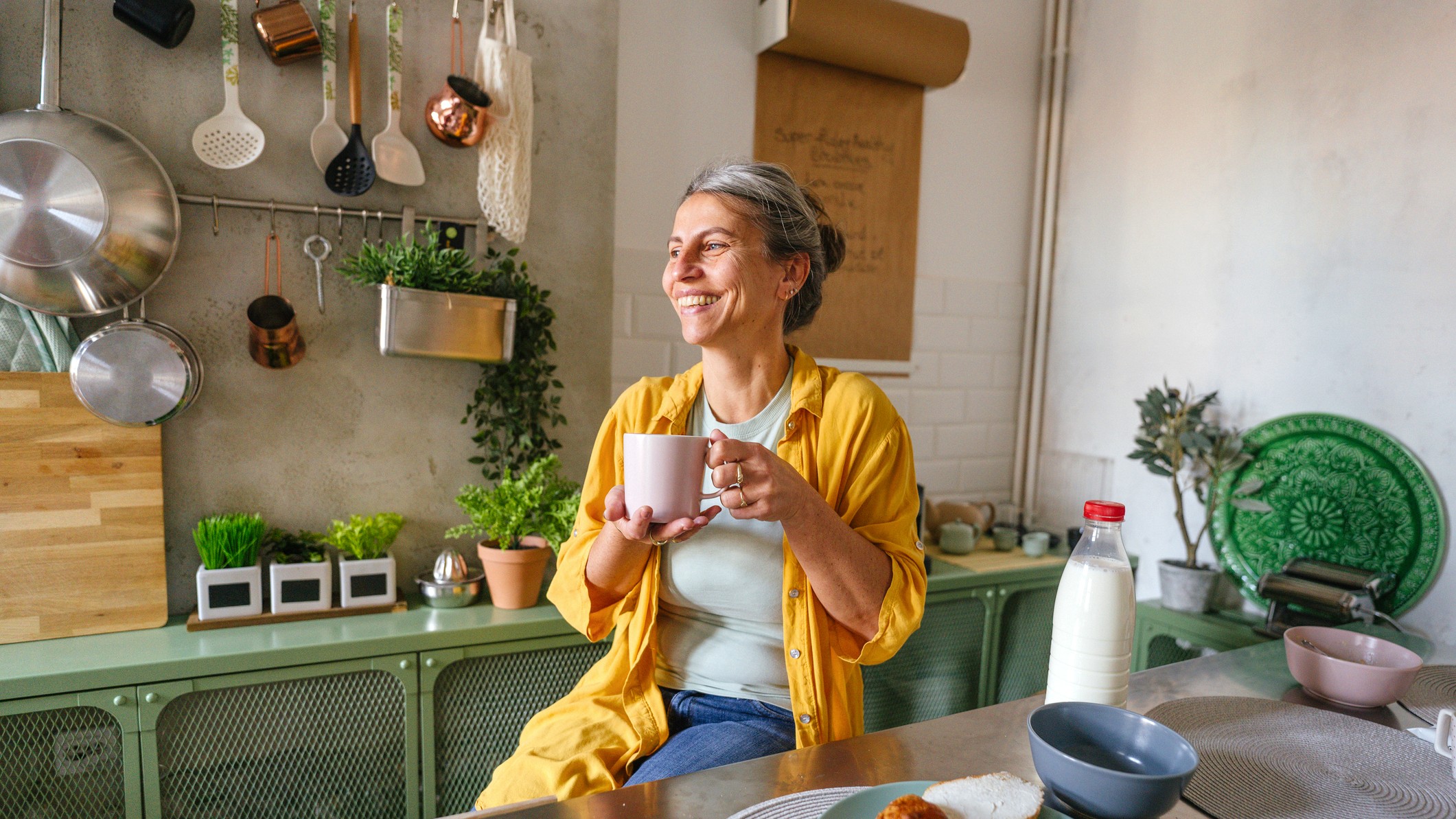 An older woman enjoying coffee in her modern, well-lit apartment kitchen.