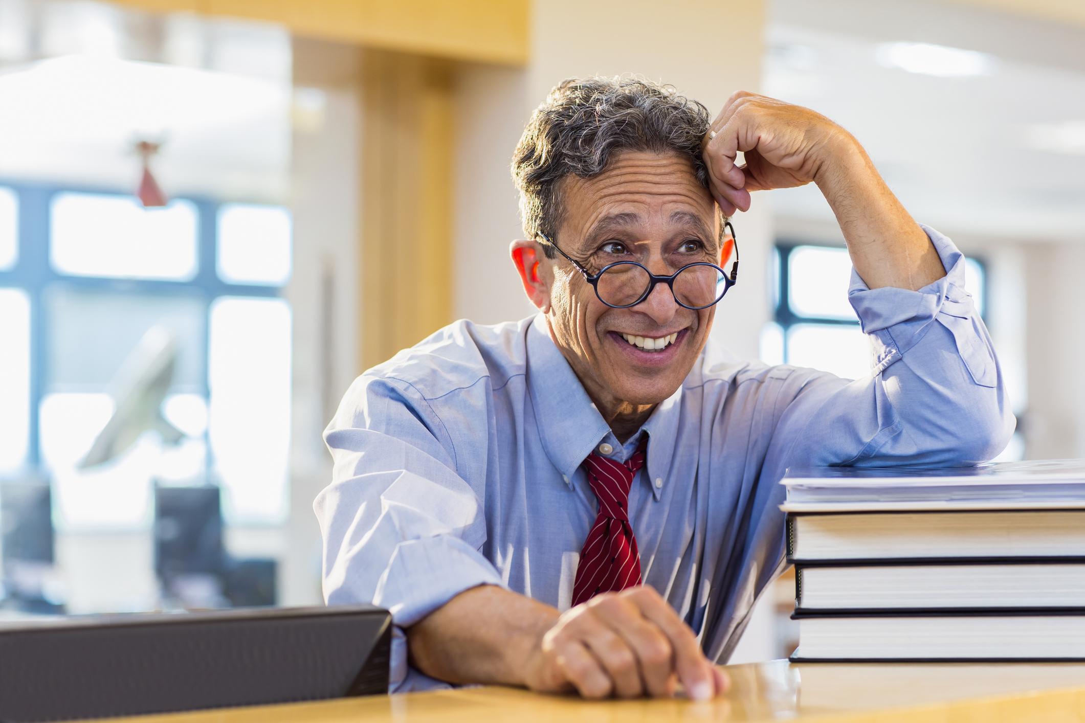 A laughing mature man with glasses and grey hair standing in a well-lit library environment.