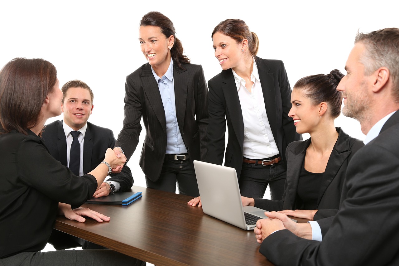 Two professionals shaking hands across a table in a bright office environment.