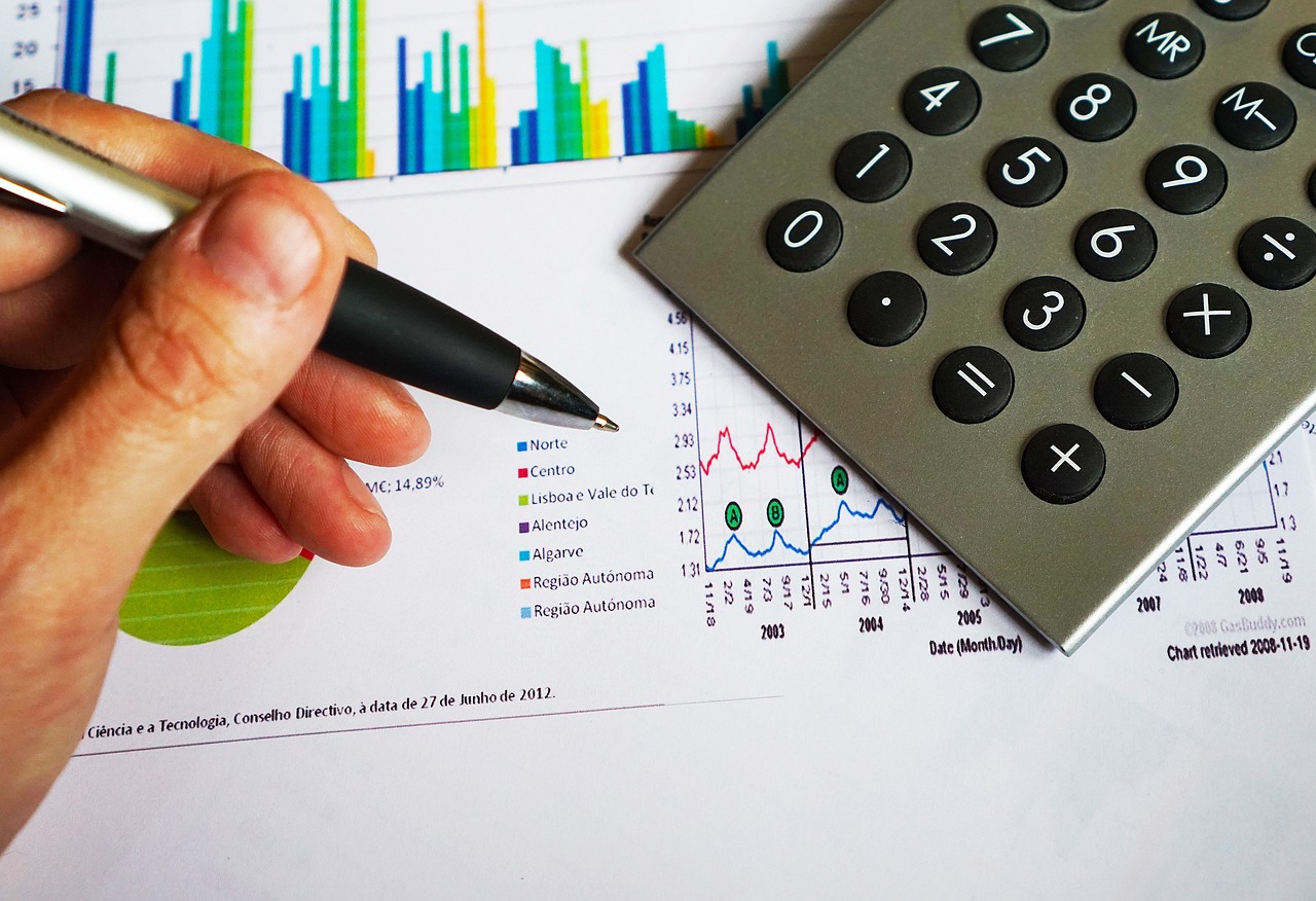 A calculator sitting next to stacked coins and a rising financial chart.