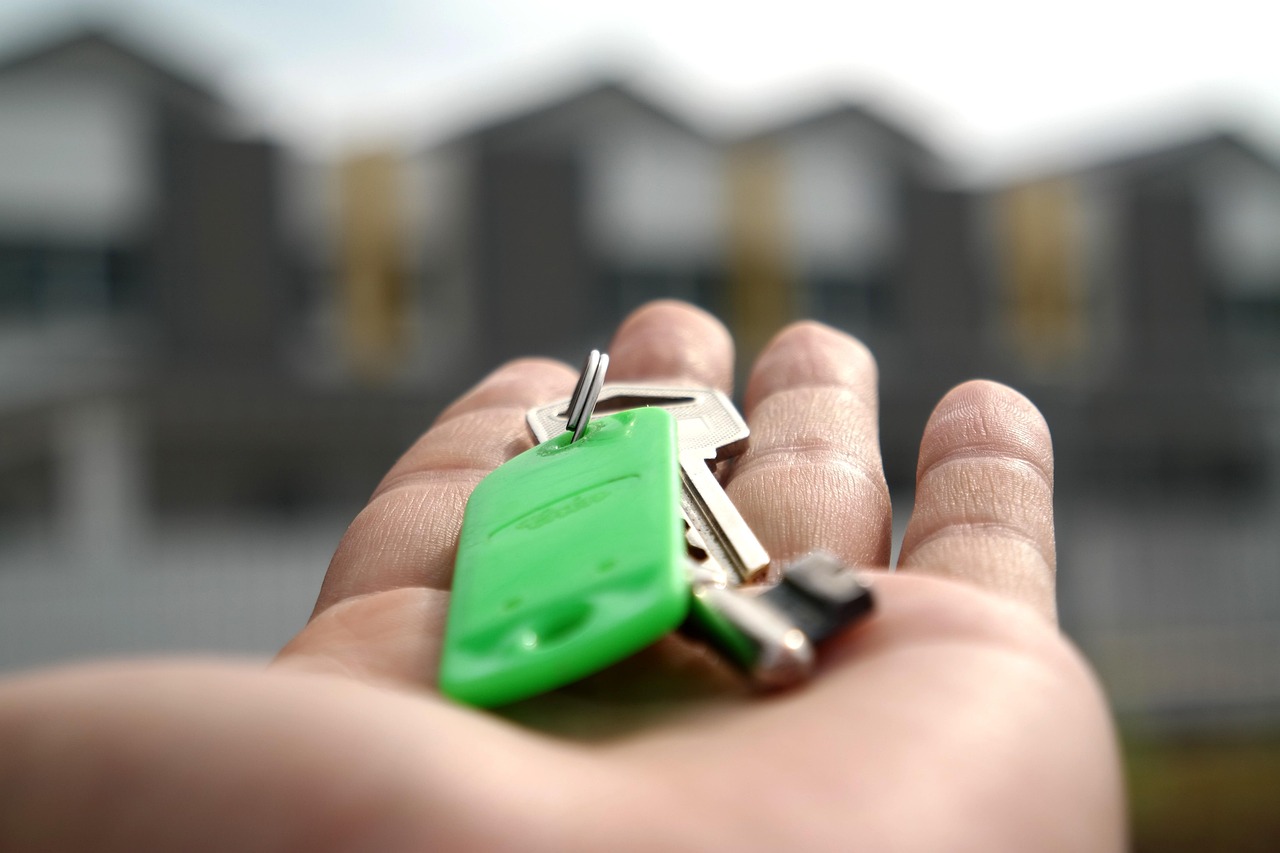 A set of house keys resting beside a small wooden house model on a light-colored surface.