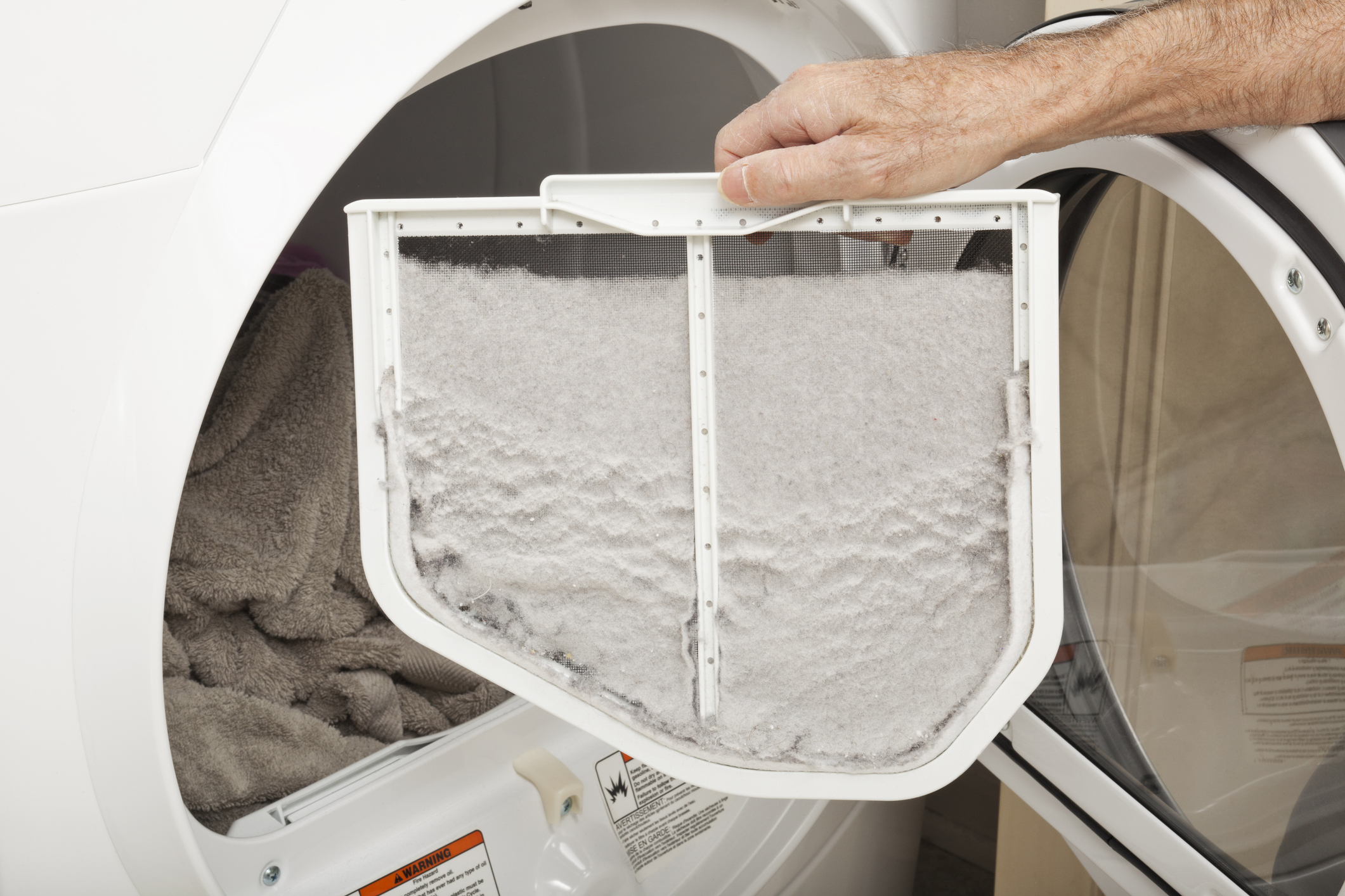 A person holding up a dryer lint filter that is heavily clogged with thick grey lint.