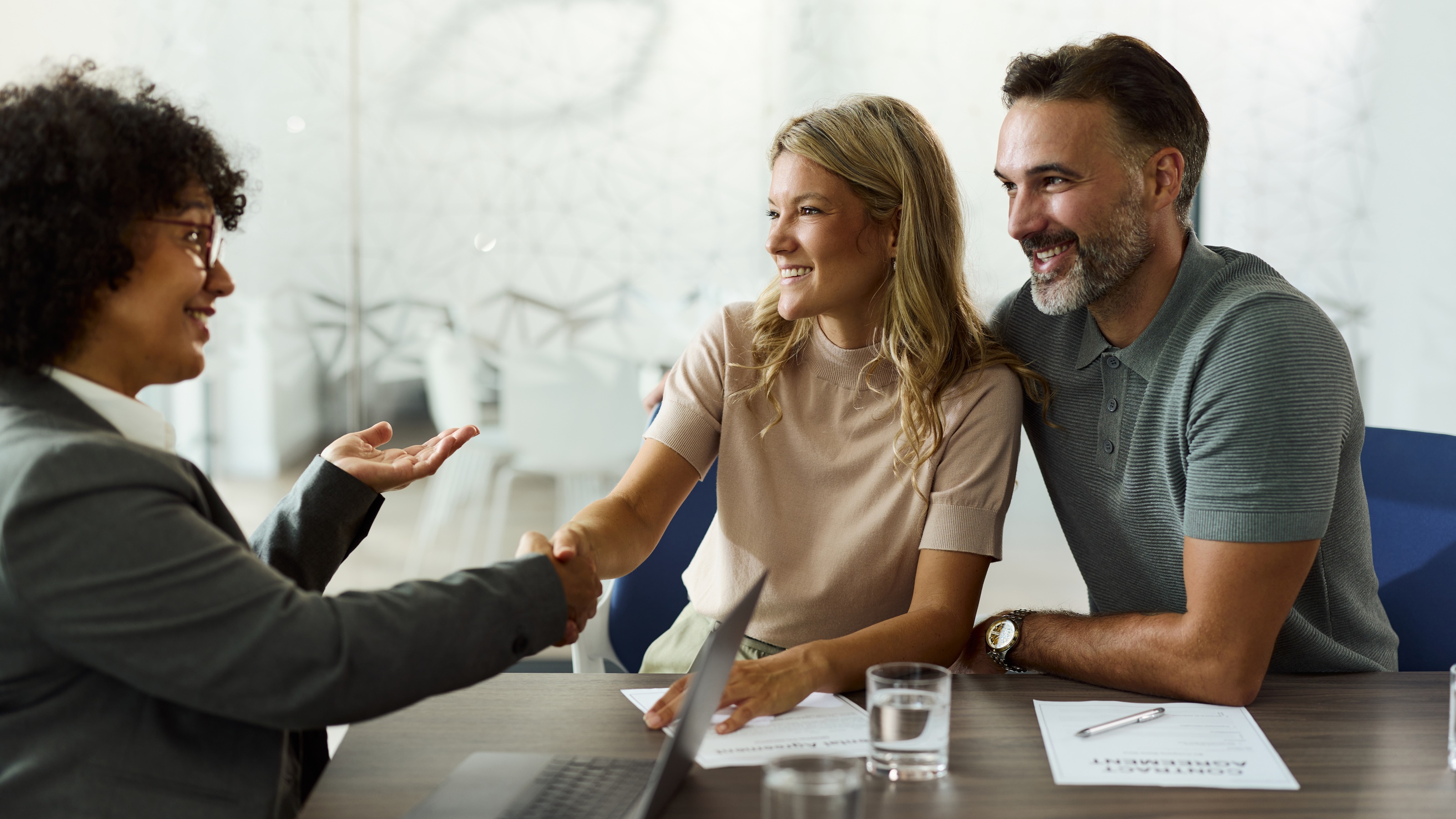 A female insurance professional shaking hands with a couple during a policy review meeting.