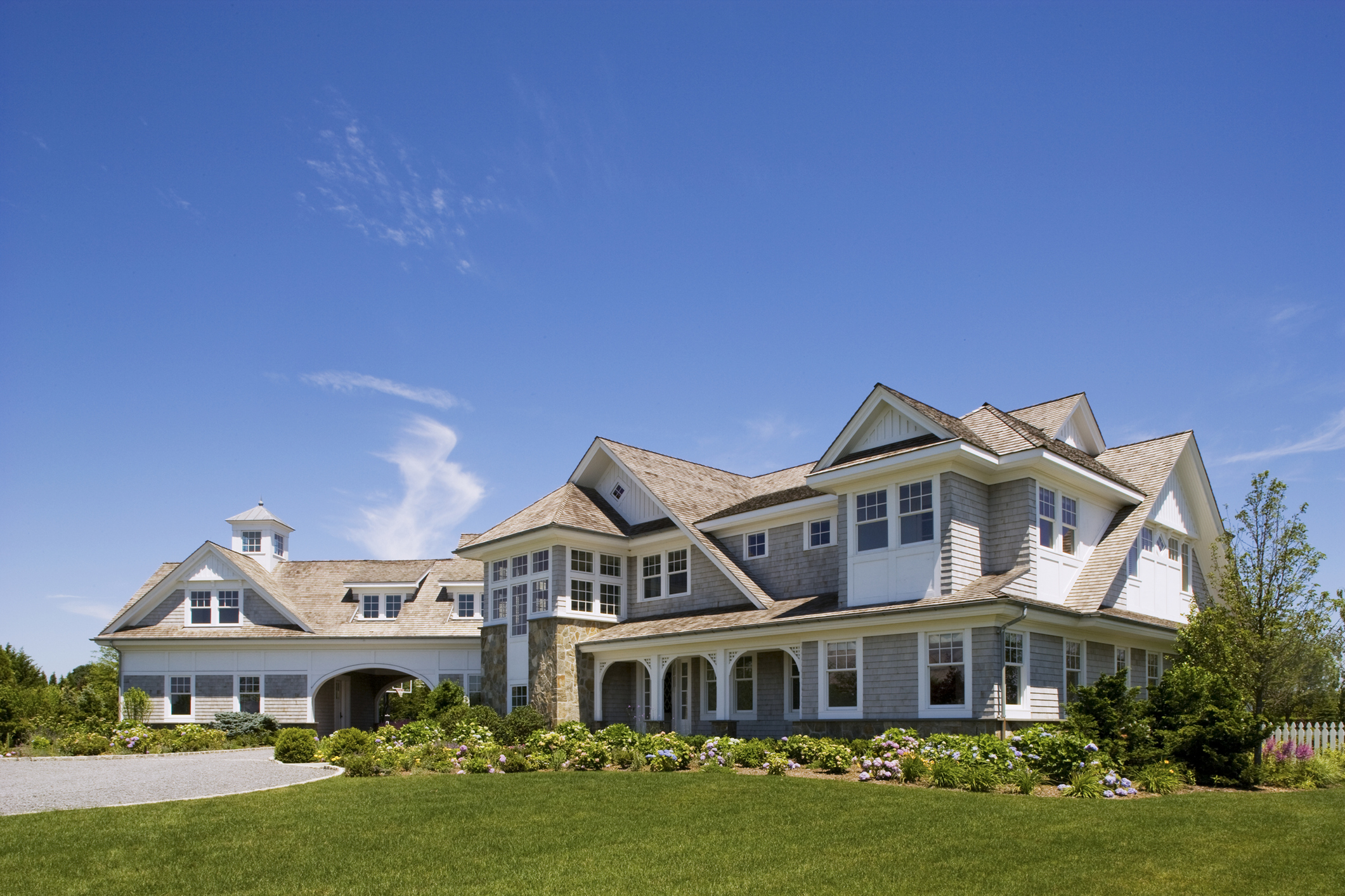 Exterior of a luxury traditional Hamptons shingled estate with a manicured green lawn.