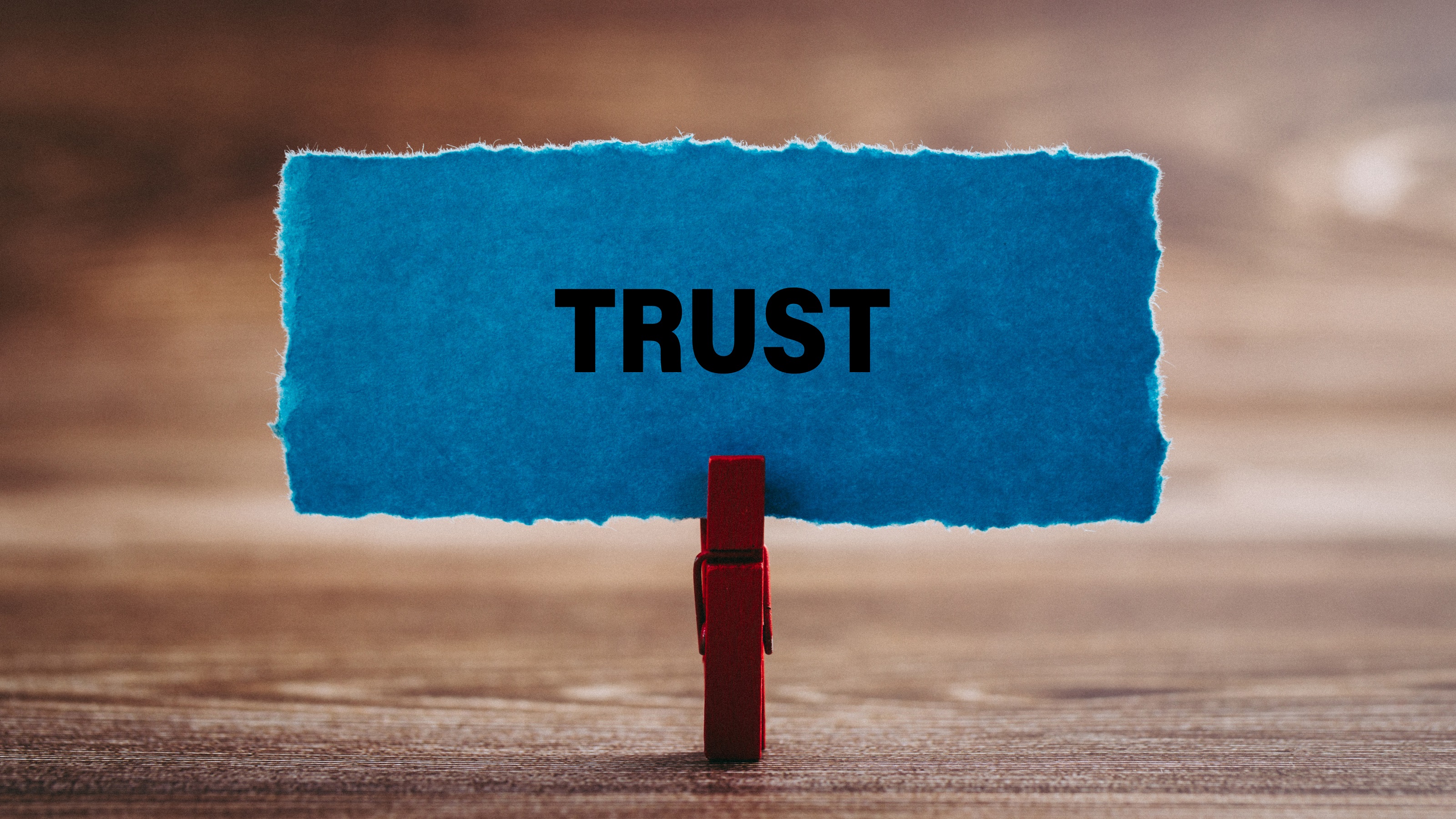 A blue piece of parchment paper with the word 'trust' written on it, held by a wooden clip.