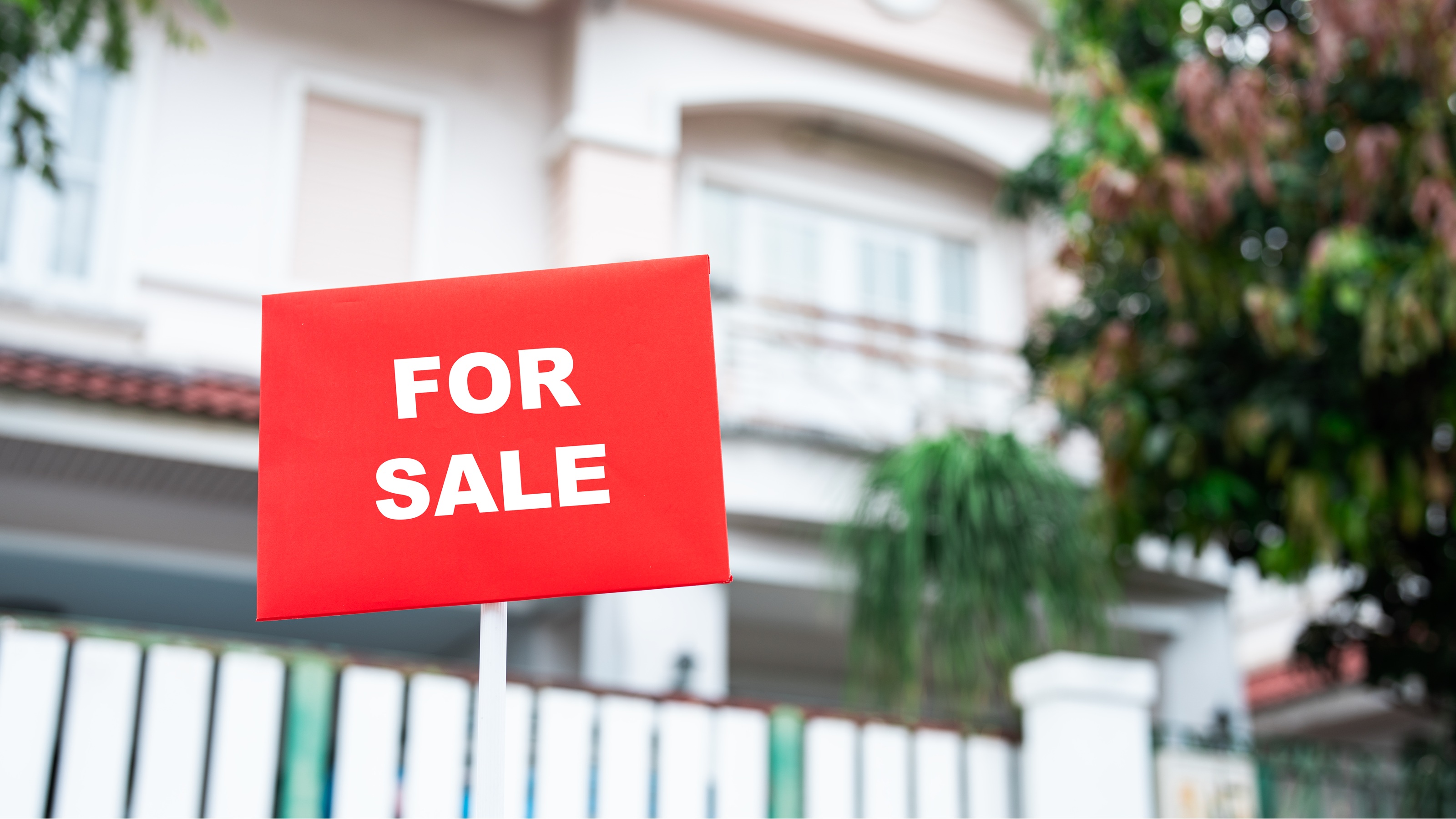 A classic for-sale sign positioned in front of a well-maintained single-family home with a white fence.