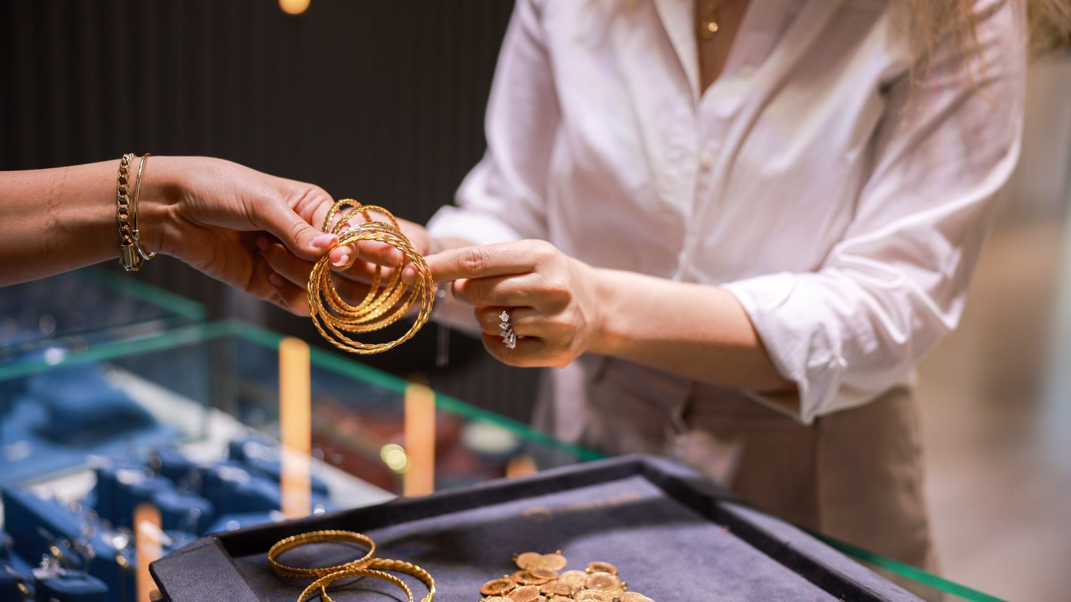 A professional jewelry store setting with a clerk showing gold accessories to a client.
