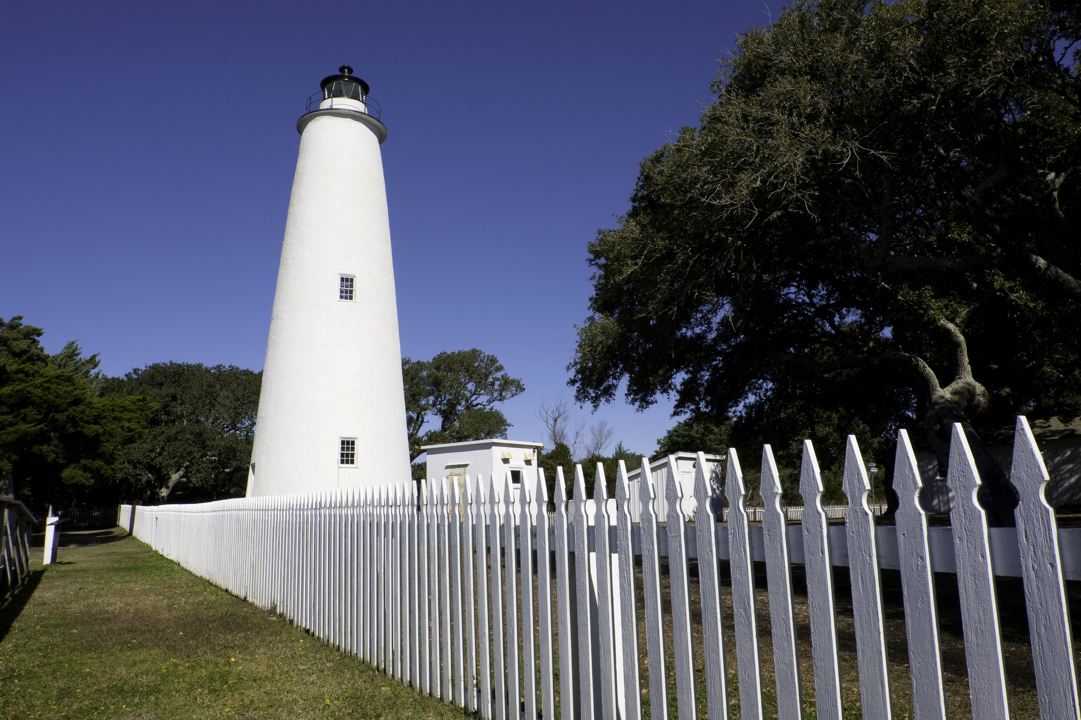 The white Ocracoke Island Lighthouse behind a white picket fence on the Outer Banks.