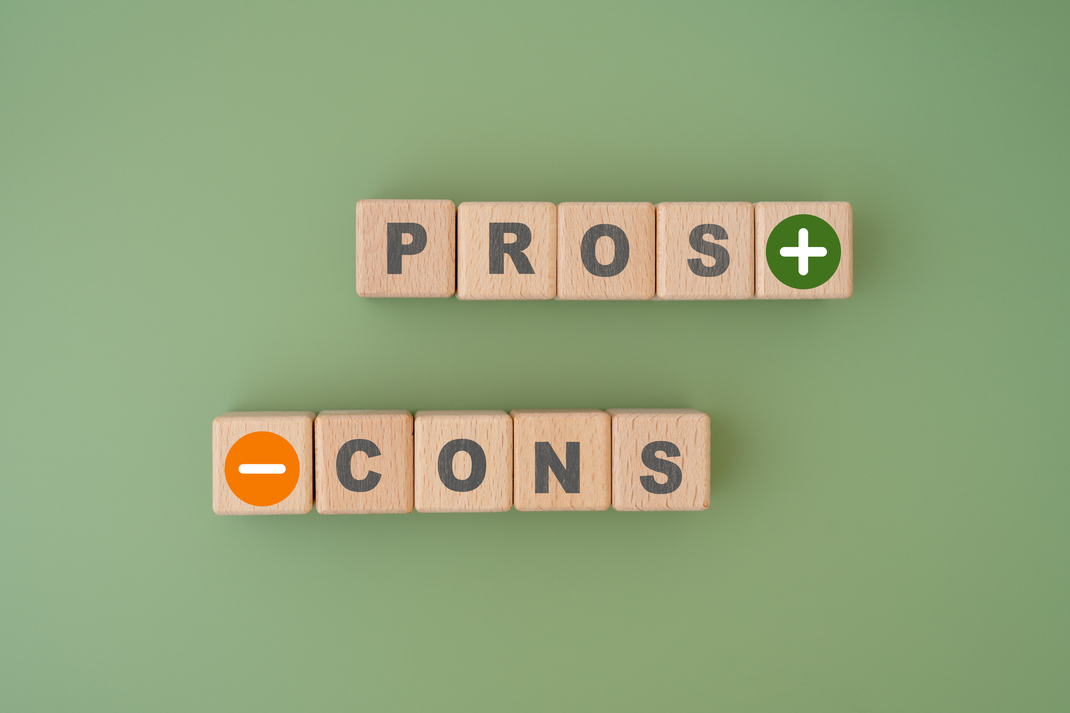 Wooden blocks spelling out 'Pros' and 'Cons' on a green background.